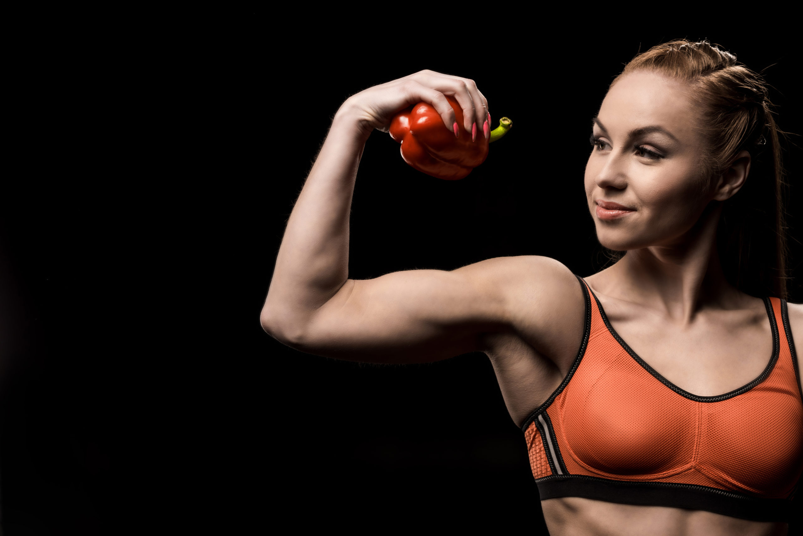 A woman demonstrating her strength by flexing her biceps with healthy food in her hand.