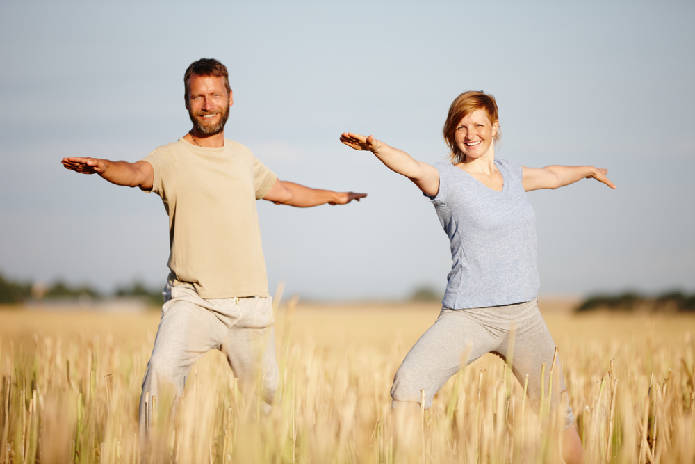 yoga is part of their lifestyle. a mature couple in the warrior position during a yoga workout in a field.